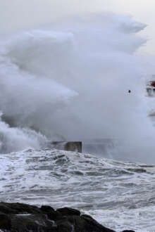 Uma onda forte a bater num rochedo, num dia fechado.